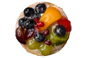 Delicious fresh tart with blueberries, cherries, grapes on a black ceramic plate photo