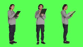 Asian adult reading information on files, thinking about annotations on clipboard papers or taking notes for finalization. Young guy writing on documents, standing against greenscreen. video