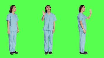 Medical assistant presents good sign over full body greenscreen backdrop, showing agreement and like gesture. Healthcare employee in uniform doing approval sign in studio. video