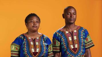 Unsure african american people doing i dont know sign in studio, showing doubtful clueless gesture on camera. Man and woman being uncertain, posing over orange background. video