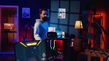 Man arriving in gaming room, ready to play science fiction videogame on PC with his friends. Gamer using headphones microphone to talk with internet teammates in online coop shooter video