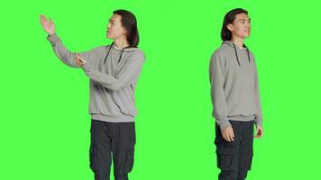 Asian man creates advertisement in studio, pointing to left or right sides for new marketing slogan campaign. Young person smiling and working on promotional ad, standing over greenscreen. video