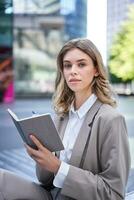 A young woman in corporate suit, sits with notebook and pen, takes notes, works and writes down her ideas photo