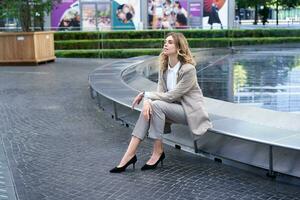 Beautiful female corporate woman in suit, sitting alone near fountain in business centre photo