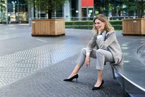 Smiling female entrepreneur in suit, lady on her lunch break waiting for someone near fountain on empty street photo