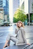 Vertical portrait of confident businesswoman, young female office worker in suit, looking at camera, sitting in city center photo