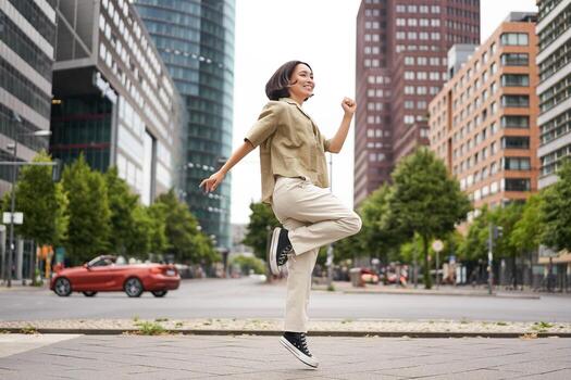 retrato de asiático contento niña saltando y bailando en ciudad centro, posando en calles, Rápido alegría y emoción foto