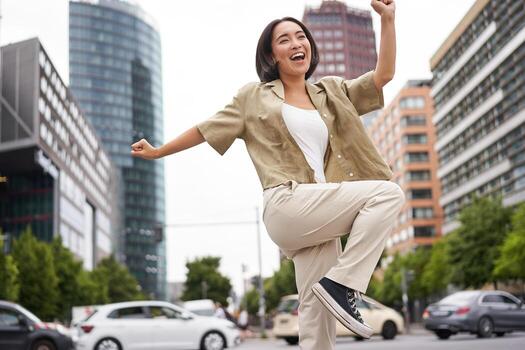 retrato de bailando asiático mujer, levantamiento manos arriba y sensación feliz, posando en ciudad, triunfando, sensación alegría foto