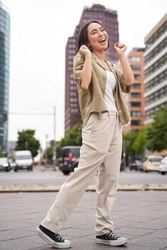 vertical Disparo de joven asiático mujer posando feliz, levantamiento manos arriba y baile, triunfando, celebrando victoria, disfrutando día fuera en ciudad foto