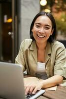 Smiling young woman working from cafe or co-working space, sitting with laptop, studying or doing homework, looking happy photo