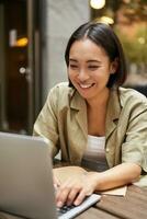 Smiling young woman working from cafe or co-working space, sitting with laptop, studying or doing homework, looking happy photo