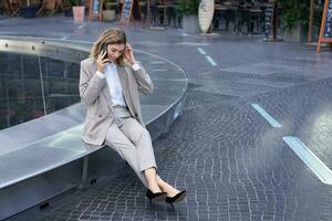 Young female manager. Corporate woman sitting outside on street and talking on mobile phone. Girl making phone call photo