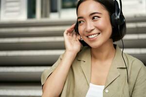 Portrait of beautiful girl in earphones, listening music, smiling and walking in city centre photo