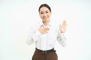 retrato de hermosa asiático mujer levanta uno mano, sonrisas amigable, presenta sí misma, saluda y dice Hola, blanco antecedentes foto