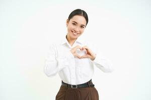 Smiling businesswoman shows heart sign with care and tenderness, stands over white background photo