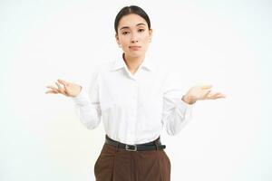 Clueless asian corporate woman, shrugs shoulders with puzzled face expression, stands confused, white background photo