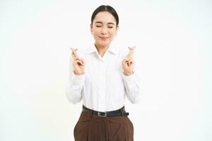 Hopeful young aspiring woman, businesswoman cross fingers for good luck, makes wish, hopes for something, white background photo