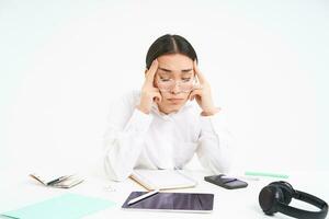 Workplace and business. Portrait of tired woman in office, company employee sits at desk with exhausted face, touches her head, has headache, white background photo