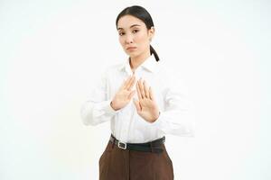 Stop, stay back. Young asian woman rejects smth, pulls away, holds hands extended to refuse, disapprove something, white background photo