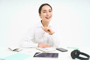 retrato de exitoso mujer de negocios, oficina gerente a lugar de trabajo, se sienta con digital tableta y su trabajando documentos, usa anteojos, sonrisas a cámara foto