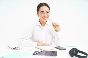 Office work and business. Young professional female employer, team leader sitting at workplace with digital tablet, smiling at camera, white background photo