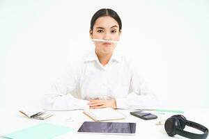 Business and office work. Young woman sitting at workplace, fooling around, holds pen with lips and shows funny faces, white background photo