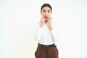 Corporate woman looks amazed, holds hands near face with surprised face expression, isolated on white background photo