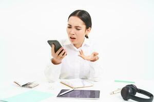 Angry lady boss, businesswoman looks frustrated, talks on mobile phone, has an argument during conversation on cellphone, sits in her office, white background photo