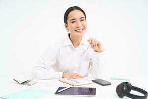 retrato de exitoso mujer de negocios, oficina gerente a lugar de trabajo, se sienta con digital tableta y su trabajando documentos, usa anteojos, sonrisas a cámara foto