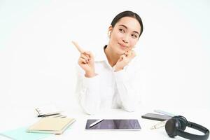 Portrait of asian businesswoman sits in office with tablet, points left and smiles, shows advertisement, office banner, white background photo