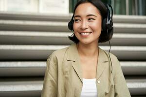 Portrait of beautiful girl in earphones, listening music, smiling and walking in city centre photo