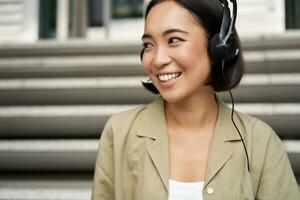 Portrait of beautiful girl in earphones, listening music, smiling and walking in city centre photo