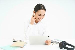 Portrait of korean businesswoman in headphones, connects to meeting on digital tablet, talks on video chat, joins online conference, white background photo