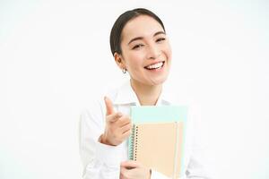 Portrait of korean teacher, female tutor shows thumbs up and laughs, holds notebooks, stands over white background photo