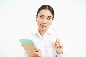 Confident young woman, office worker with glasses, holds notebooks, looks thoughtful, thinking, standing isolated on white background photo