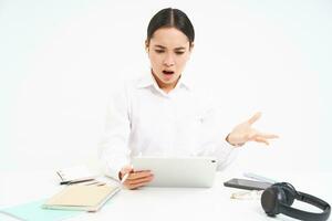 Angry korean woman shouting at employee on video chat, has intense conversation online, looks frustrated at digital tablet, white background photo