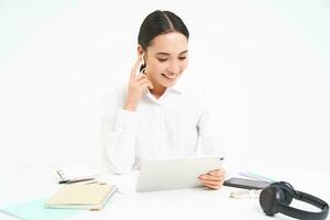 Portrait of korean businesswoman in headphones, connects to meeting on digital tablet, talks on video chat, joins online conference, white background photo