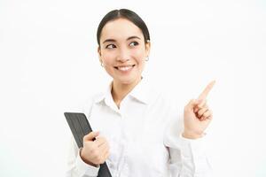 Image of young professional woman, pointing finger right, holding digital tablet, showing advertisement campaign, isolated on white background photo