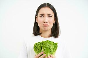 Crying woman holding vegetable, sitting on diet and eating cabbage instead of junk food, white background photo