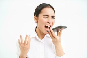 Angry korean saleswoman, shouting at smartphone speaker, screaming at mobile phone, scolding employee on cellphone, white background photo