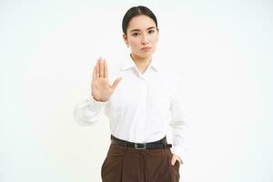 Stop. Strict and serious lady boss, asian woman shows extended hand, rejection, prohibit gesture, white background photo