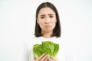 Crying woman holding vegetable, sitting on diet and eating cabbage instead of junk food, white background photo