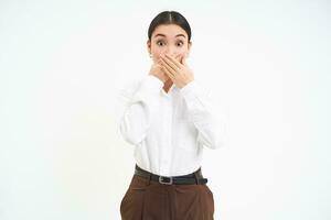 Image of shocked saleswoman, covers her mouth with hands and looks astonished at camera, white background photo