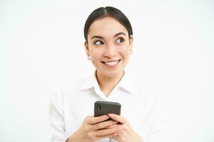 Image of asian saleswoman, office manager holding smartphone, working on text for social media, using cellphone, white background photo