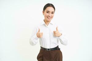 Smiling asian woman shows thumbs up, approves promo offer, recommends product, stands isolated over white background photo