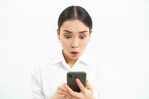 Portrait of korean businesswoman with worried face, reading message on mobile phone screen, isolated on white photo