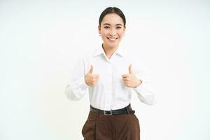 Smiling asian woman shows thumbs up, approves promo offer, recommends product, stands isolated over white background photo