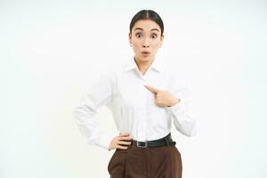 Portrait of asian woman looks surprised, points at herself with amazement, white background photo