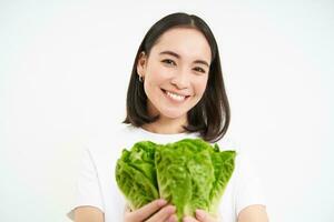 Smiling cute young woman shares her lettuce with you, gives cabbage for person on diet, white background photo