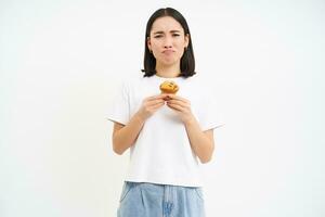 Portrait of miserable girl with cupcake, sad without sweets, cant eat pastry, being on diet, white background photo